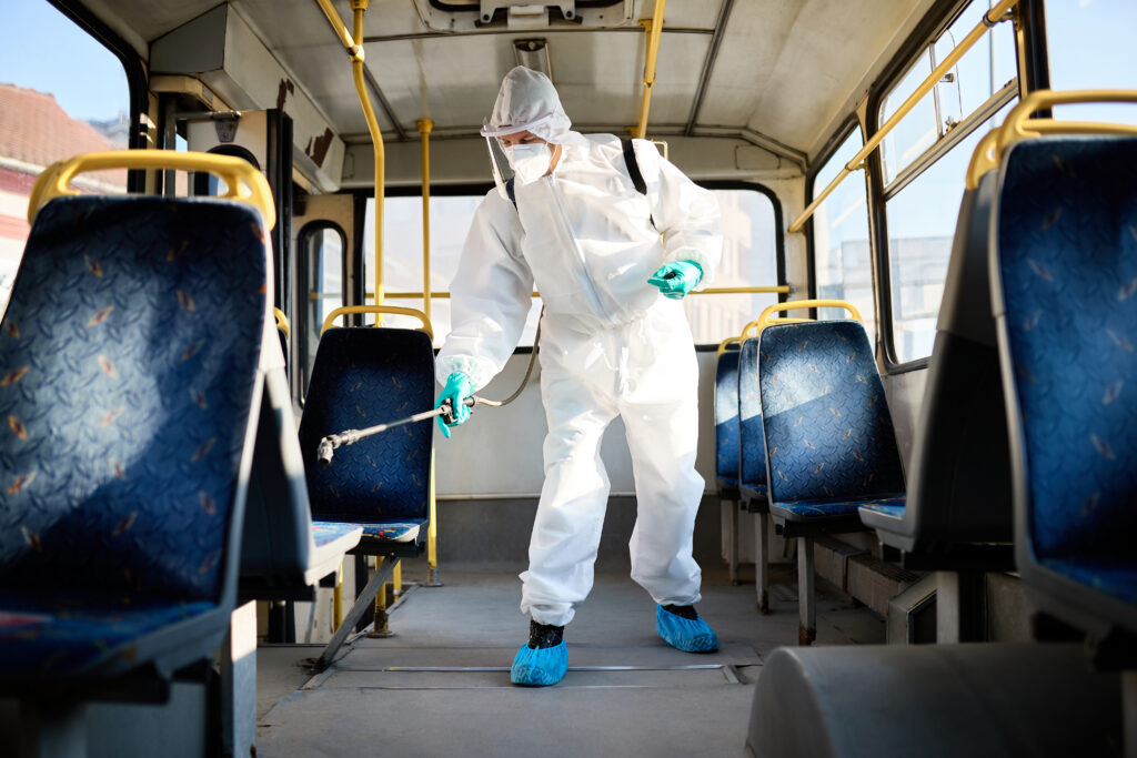 Disinfectant worker spraying inside of a public bus due to coron